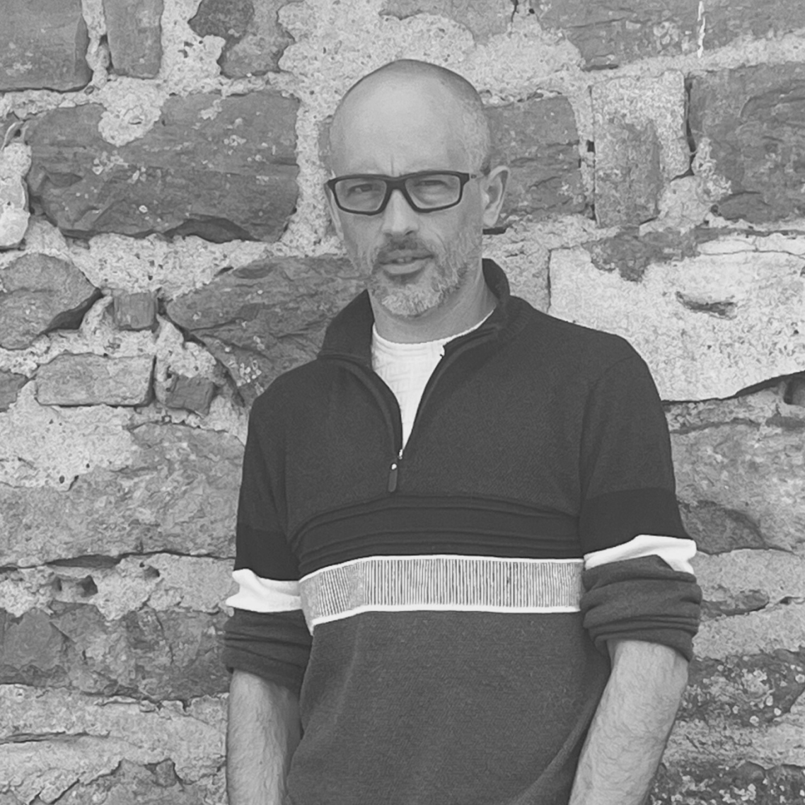 Jérôme Guilloux en noir et blanc, devant un mur en pierre, style professionnel – Qui suis-je Loany